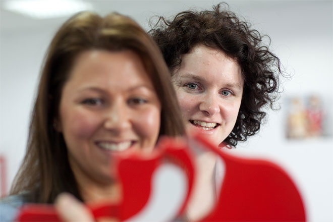 Foto: Zwei Kursteilnehmerinnen blicken motiviert auf ein Kopfschnittmodell, das die DRK-Kursleiterin zur Veranschaulichung in Händen hält. Es soll verdeutlichen, wieso das Überstrecken des Kopfes bei bewusstlosen Personen lebensrettend sein kann.