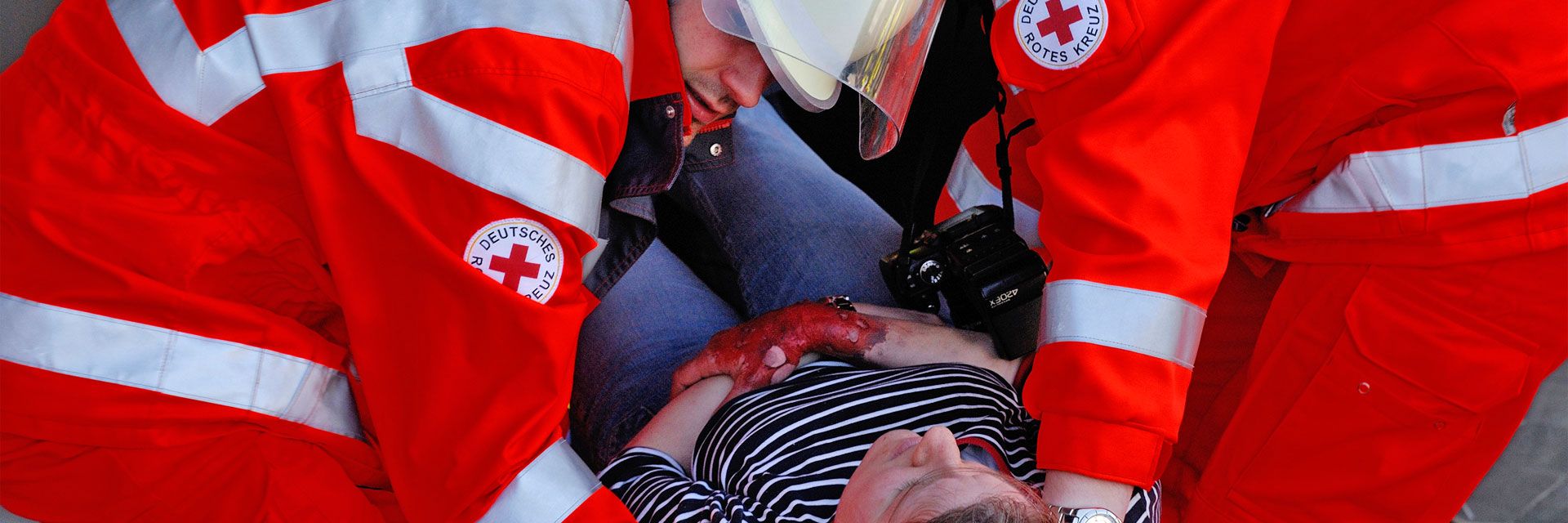 Foto: Bei einer Helferübung zum Thema Brandanschlag tragen zwei DRK-Einsatzkräfte eine Frau aus der Gefahrensituation. Sie stützen vor allem den Kopf der Frau.